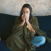 Woman sneezing while sitting, showing symptoms of viral cold